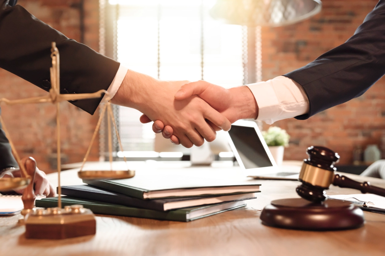 Lawyers exchanging handshake beside scales and gavel