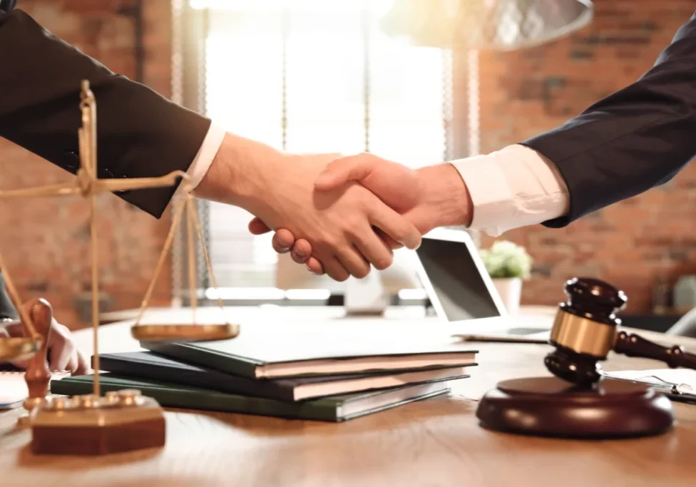 Lawyers exchanging handshake beside scales and gavel